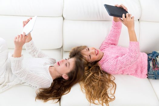 Children friends kid girls having fun playing with tablet pc lying on white sofa