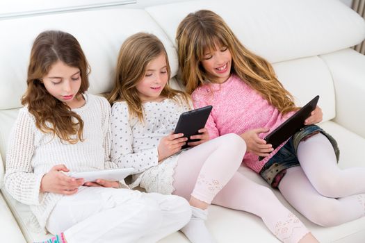 three kid sister friends girls group playing together with tablet pc on white sofa