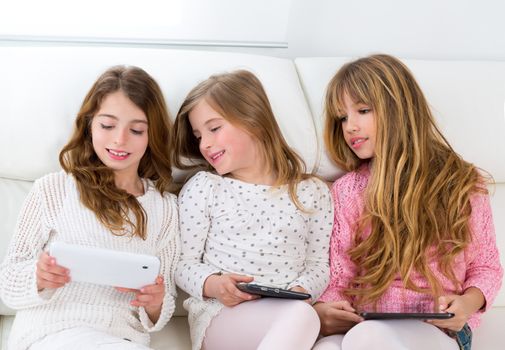 three kid sister friends girls group playing together with tablet pc on white sofa