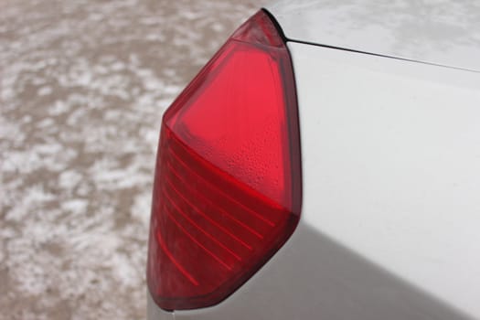 bright red taillight silver car on a background of snow-covered roads