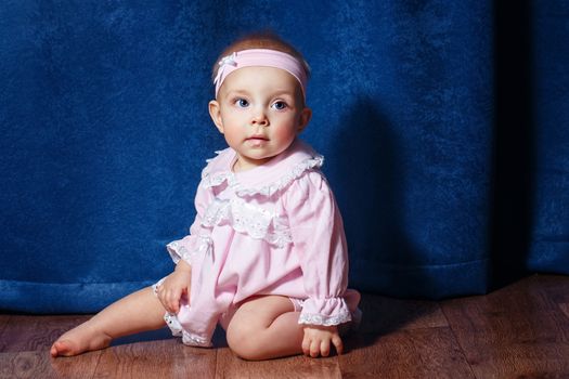 Cute little girl in a pink dress sitting on the floor barefoot