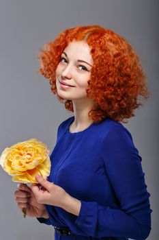 Attractive young red-haired girl in a blue dress holding in her hands a yellow flower