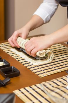 Hands of woman chef rolling up a japanese sushi with rice, avocado and shrimps on nori seaweed sheet