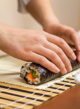 Hands of woman chef rolling up a japanese sushi with rice, avocado and shrimps on nori seaweed sheet