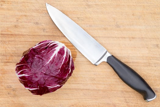 Overhead view of a single cleaned whole raw red radicchio displayed with a kitchen knife on an old bamboo cutting board with copyspace during preparation in the kitchen