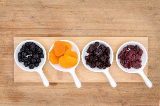 Mixed dried fruit and berries in ceramic ramekins including apricots, cherries, blueberries and cranberries rich in antioxidants and vitamins, overhead view on a bamboo cutting board