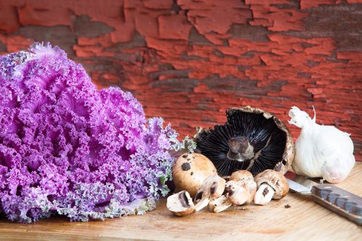 Purple curly-leaf kale, agaricus mushrooms and garlic in a rustic kitchen on a bamboo chopping board with a knife waiting to be prepared for a healthy savoury meal