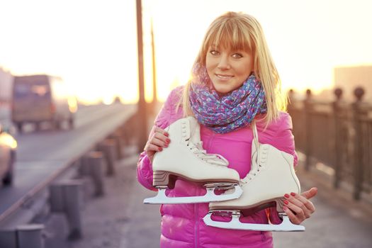 Beautiful smiling blond woman with ice skates on the bridge