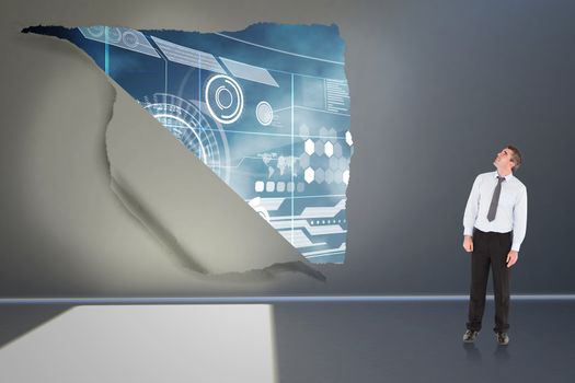 Businessman looking up against rip on wall showing technology interface