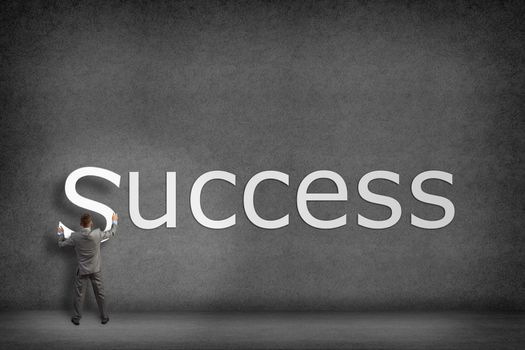 Businessman collects on the wall the word success, places the letter on the wall