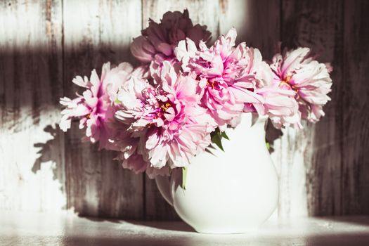 Still life with peonies over shabby wooden wall with sunlight from window