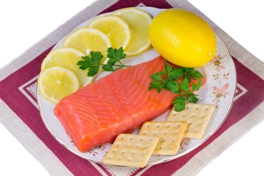 On a platter lie salmon fillet, lemons, sliced and whole, biscuits, fresh herbs parsley. Presented on a white background.