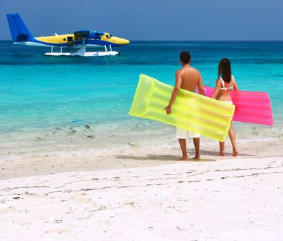 Couple with inflatable rafts looking at arrived seaplane on a tropical beach at Maldives. No brand names or copyright objects