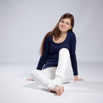 Young long-haired woman without makeup in white jeans and a blue shirt sitting on the floor