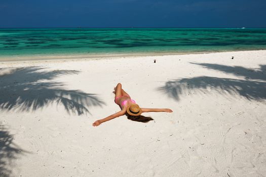 Woman in bikini at tropical beach under the palm tree shadow