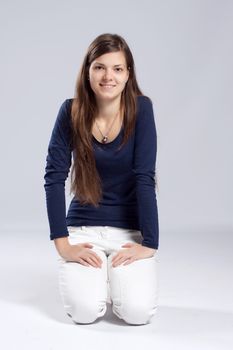 Young long-haired woman without makeup in white jeans and a blue shirt, kneels on the floor