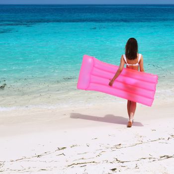 Woman with pink inflatable raft walking at the beach