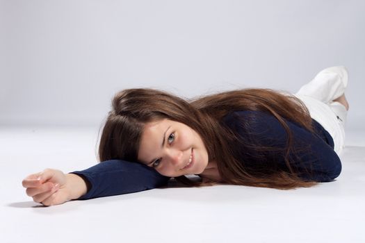 Young long-haired woman without makeup in white jeans and a blue shirt lying on the floor