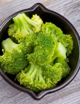 Crunchy Boiled Broccoli in Black Stew Pan closeup on Wooden background. Top View