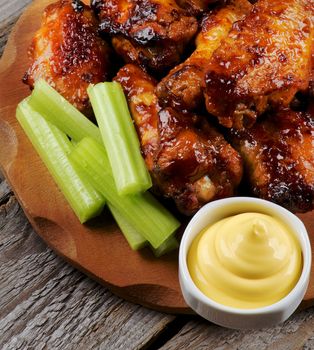 Arrangement of Celery Sticks, Cheese Sauce and Barbecue  Chicken Legs and Wings Barbecue closeup on Wooden Plate