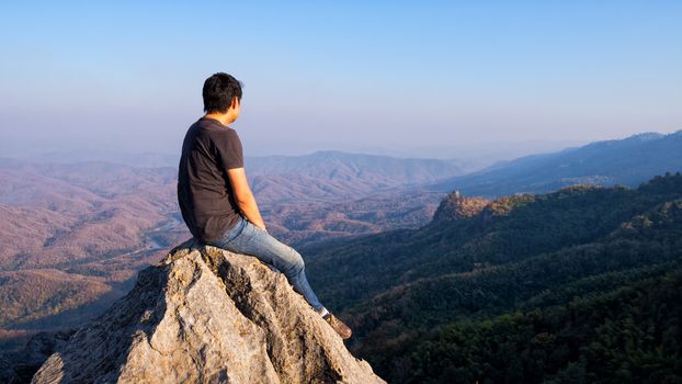 man sitting on stone top of high mountain