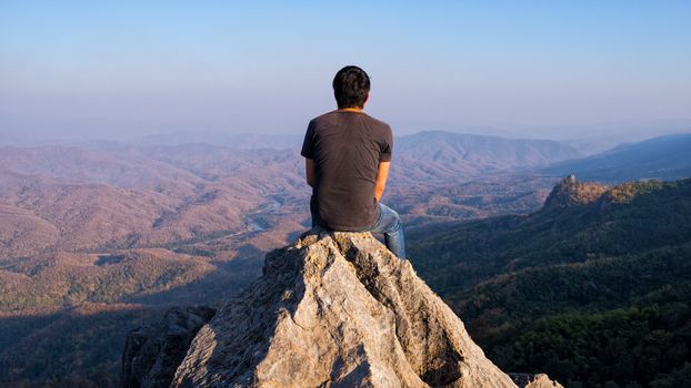 man sitting on stone top of high mountain