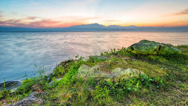 twilight time sunset behind mountain with lagoon  stone and grass in front of view motion blur of water in thailand