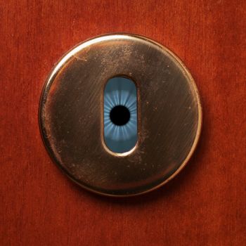 Blue eye behind a keyhole of a wooden door