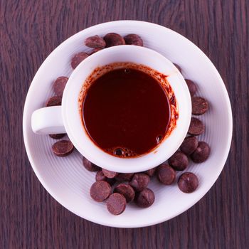 Hot Chocolate in small white cup with chocolate beans, over wooden background