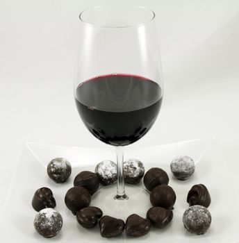 A glass of wine and assortment of chocolates on a white plate.