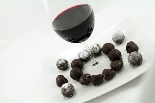 A glass of wine and assorted chocolates on a plate.