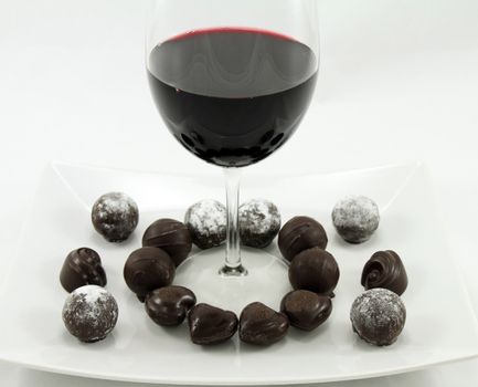 A glass of wine and assorted chocolates on a white plate.