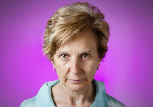 Portrait of a real serious middle aged woman over purple background