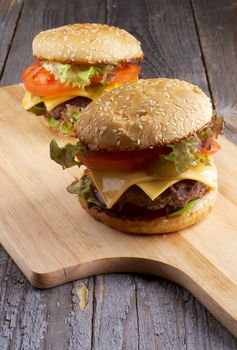 Two Tasty Hamburgers with Beef, Tomato, Lettuce, Pickle, Red Onion and Cheese into Sesame Buns closeup on Wooden Cutting Board