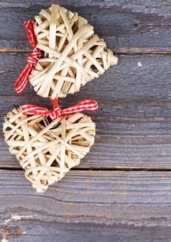 Arrangement of Two Handmade Wicker Hearts with Red Checkered Bows isolated on Rustic Wood background. Top View