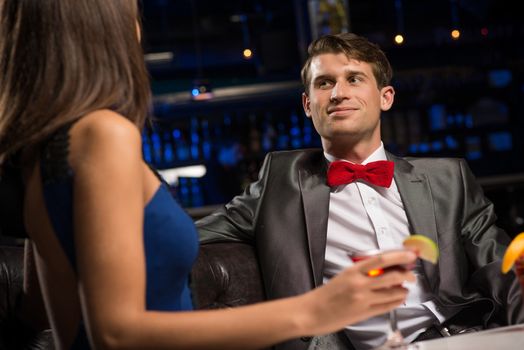 portrait of a man in a nightclub, sitting on the couch and talking with woman