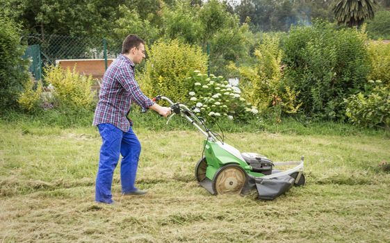 Young man mowing the lawn with a lawnmower machine