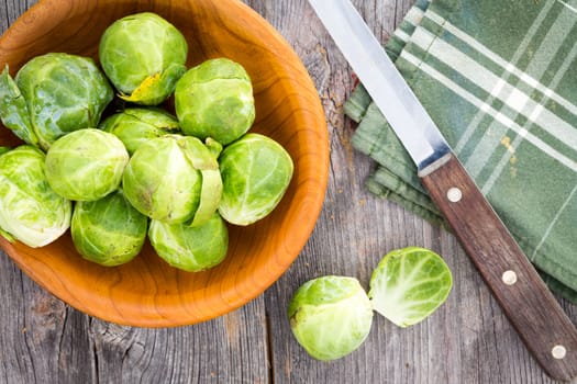 Preparing brussels sprouts for the evening meal with an overhead view of fresh healthy sprouts in a wooden dish alongside a kitchen knife and napkin on old weathered wooden boards