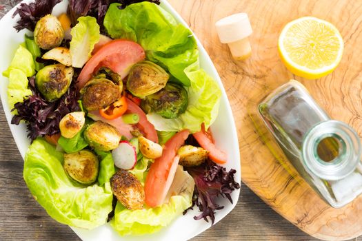 Mixed salad greens with sauteed brussels sprouts, tomato and radish drizzled with virgin olive oil and lemon dressing and served in a dish, overhead view