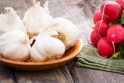 Close up view of healthy fresh whole garlic bulbs for an aromatic pungent seasoning used in cooking with a bunch of crisp red radishes on old wooden boards