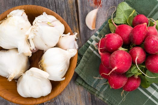 Overhead view of whole bulbs of fresh garlic in a wooden bowl with a bunch of farm fresh radishes ready to be used in preparing a healthy meal