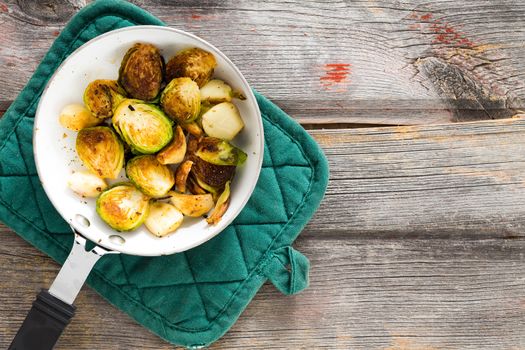 Delicious browned sauteed diced brussels sprouts in a saucepan on an oven cloth, overhead view on an old rustic weathered wooden table top with grungy boards and copyspace