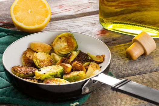 Succulent sauteed brussels sprouts cooked in tangy lemon and olive oil displayed in the saucepan on an old wooden table, close up side view