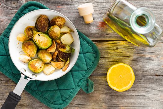 Delicious sauteed brussels sprouts with olive oil and fresh lemon for a tangy zesty flavour in a saucepan on a rustic tabletop in a country kitchen, overhead view