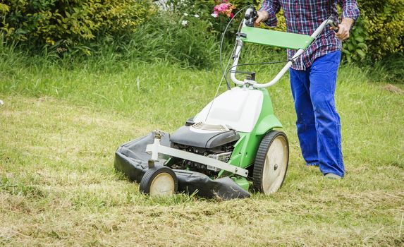 Young man mowing the lawn with a lawnmower machine