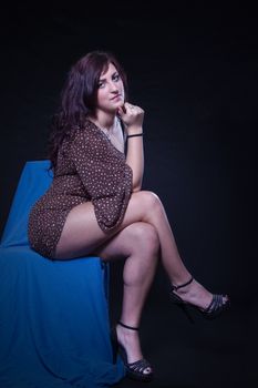 Young woman in sexy dotted mini dress sitting on a blue chair on a black background