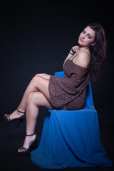 Young woman in sexy dotted mini dress sitting on a blue chair on a black background