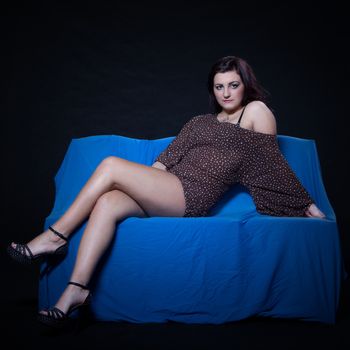 Young woman in sexy dotted mini dress lying on blue sofa on a black background