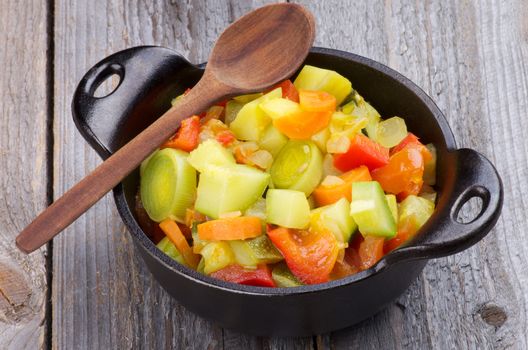 Vegetable Stew with Zucchini and Leek in Black Saucepan with Wooden Spoon isolated on Rustic background