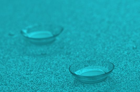 Two Contact Lenses with Water Droplets isolated on Wet background. Azure Toned.